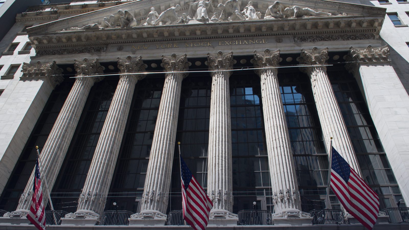 The columned facade of the New York Stock Exchange with US flags